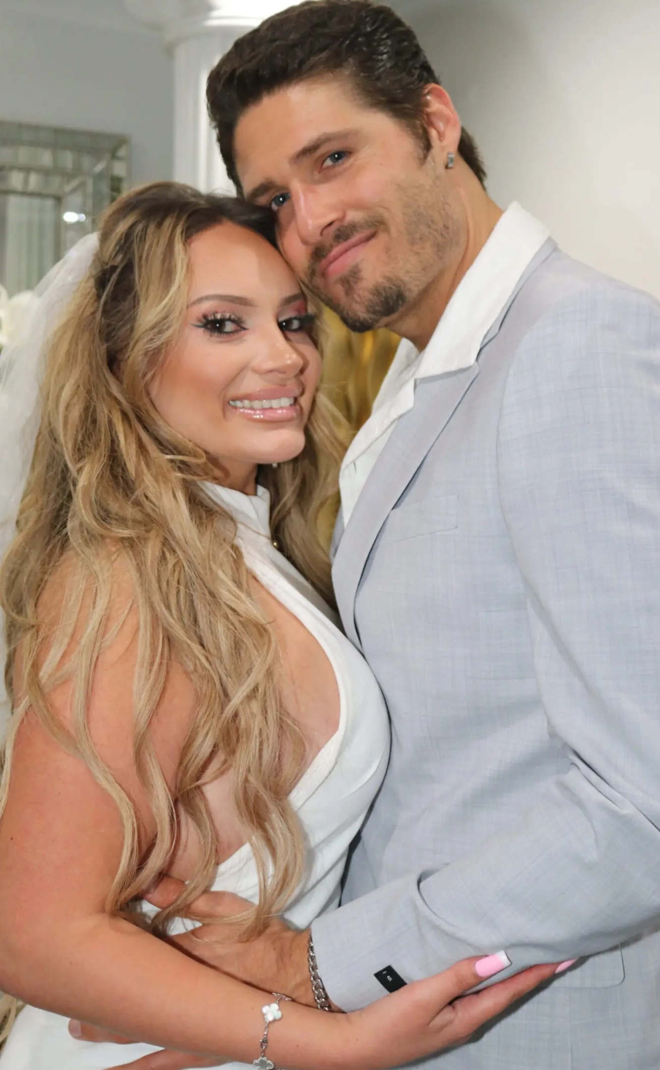 A smiling couple dressed in white and light gray, posing closely.