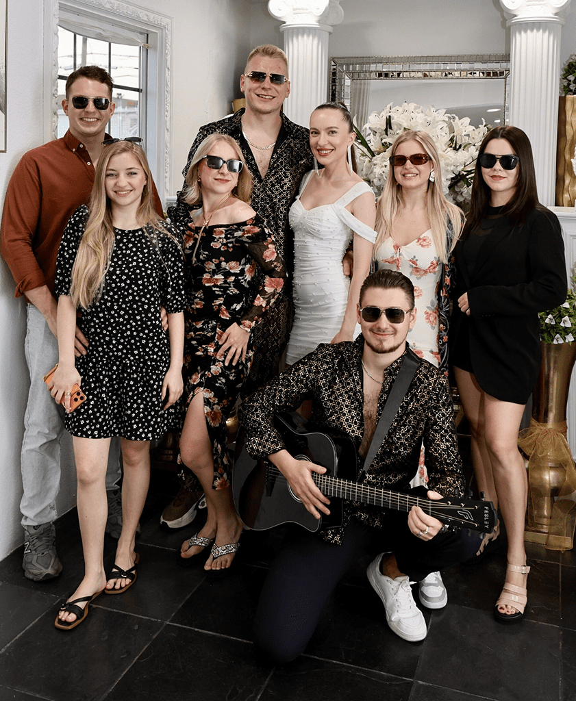 Group of friends posing in stylish outfits, one holding a guitar.