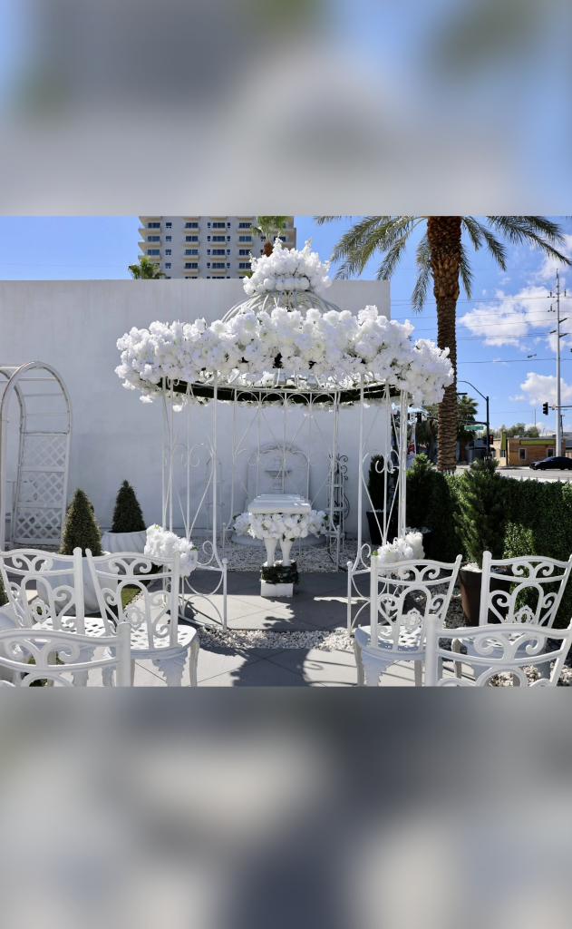Elegant outdoor wedding setup with white chairs and a floral-adorned canopy.