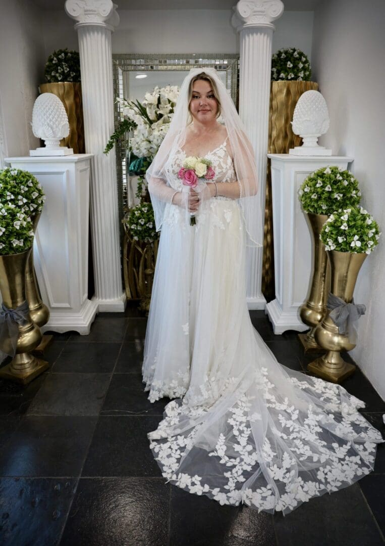 Bride in elegant white gown with long lace train holding a bouquet.