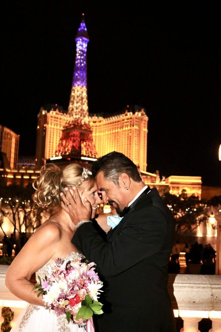 Couple sharing a romantic moment in front of a lit-up Eiffel Tower replica at night.