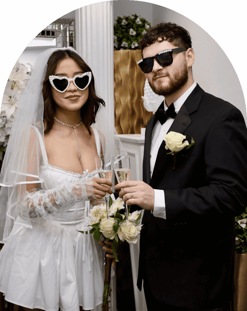 Bride and groom in stylish wedding attire holding champagne glasses.
